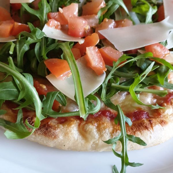 Pizza Primavera mit Mozzarella, frische Würfeltomaten, Knoblauch, Rucola, Grana Padano Flocken